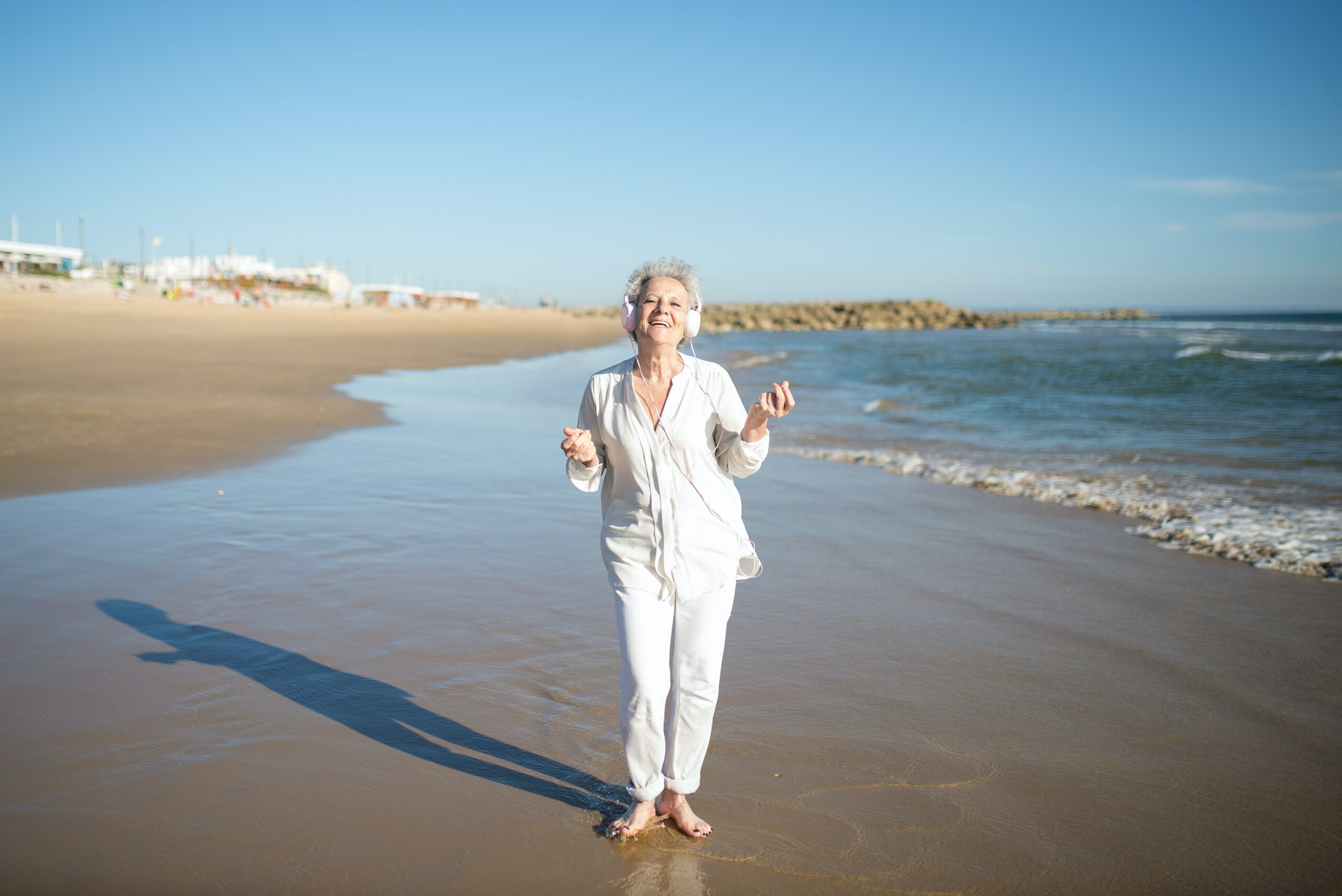 ældre-dame-på-strand-iført-hvidt-tøj-med-glad-udtryk
